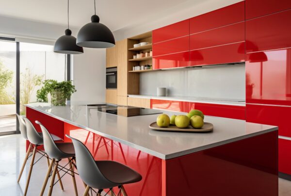 Modern custom kitchen with glossy red cabinets, sleek grey countertop island, black pendant lights, and minimalist décor featuring green apples and indoor plants.